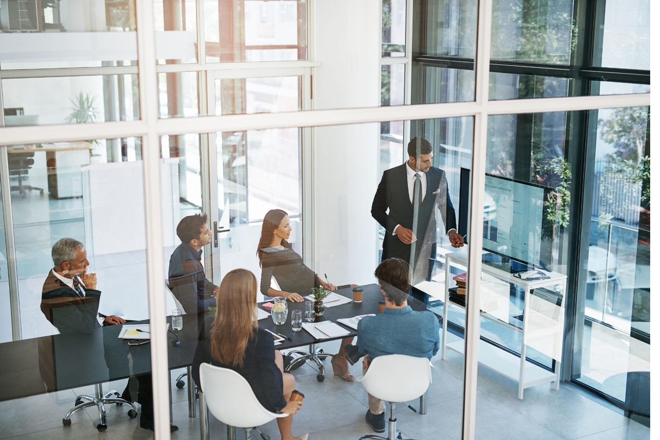 A structured team meeting, viewed through a glass office wall